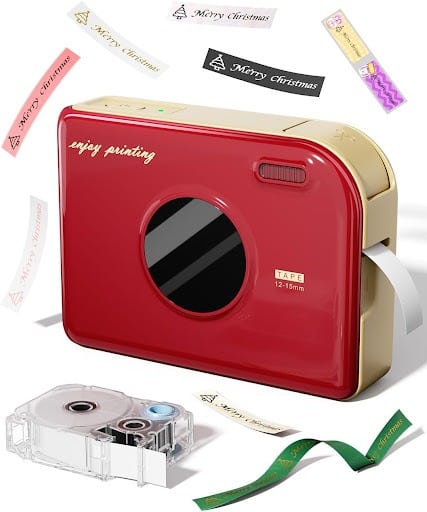 A red and beige label printer with festive tape being printed, perfect for Christmas crafts, surrounded by various holiday-themed label tapes and a clear tape cartridge nearby. "Enjoy printing" is written on the printer.