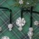 Three sparkling, vintage style Christmas ornaments with crystal designs hang from green velvet ribbons on plaid wrapping paper, surrounded by pine branches and additional brooches—perfect inspiration for a festive DIY display.