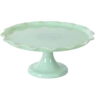 A light green, glass cake stand with a scalloped edge and a sturdy pedestal base, shown on a white background.