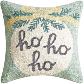 Square holiday pillow with a light green background, featuring a large white ornament, green pine branches, a yellow bow, and the words "ho ho ho" embroidered in dark gray text.