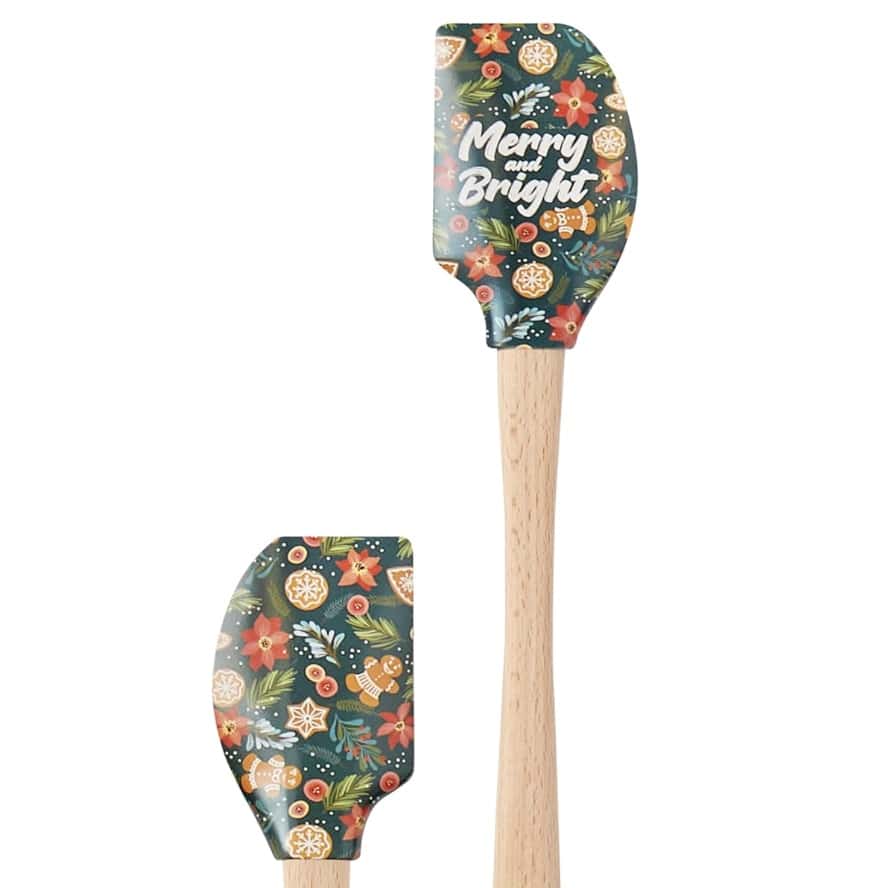 Two wooden-handled spatulas with festive designs; both have dark green silicone heads decorated with holiday elements, perfect for your favorite molded cookies recipe. The larger one reads "Merry and Bright" among gingerbread cookies, orange slices, and poinsettias.