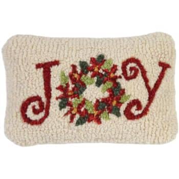 Rectangular cream-colored pillow with the word "JOY" in red; the "O" is replaced by a holiday wreath with green leaves and red berries.