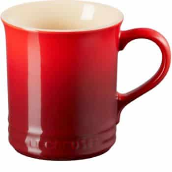 A red ceramic mug with a glossy finish and a large handle, featuring the brand name "Le Creuset" embossed near the base. The interior is a light cream color.
