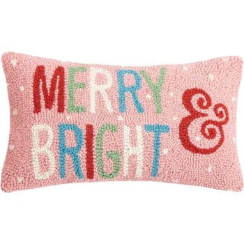 A pink rectangular pillow with white polka dots features the words "MERRY & BRIGHT" in colorful, textured letters.