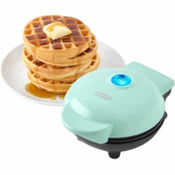 A teal mini waffle maker sits next to a plate with a stack of waffles topped with butter and syrup.