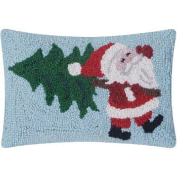 Rectangular pillow with a hooked design of Santa Claus in a red suit carrying a green Christmas tree over his shoulder on a light blue background.