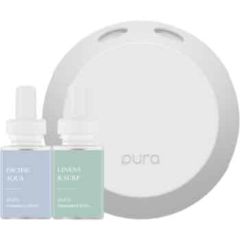 A white Pura fragrance diffuser is shown with two fragrance refill bottles labeled "Pacific Aqua" and "Linens & Surf." The bottles have pastel blue and green labels and dropper tops, and are placed in front of the diffuser.