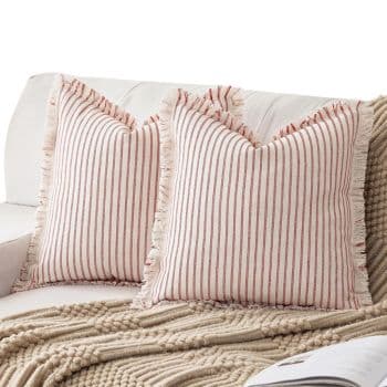 Two striped throw pillows with fringed edges rest on a light-colored sofa, next to a textured beige blanket and an open book.