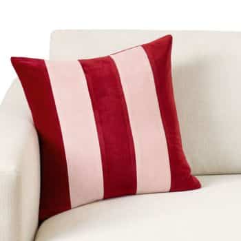 A square throw pillow with bold vertical red and light pink stripes rests against the arm of a light-colored sofa.