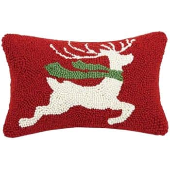 A rectangular red pillow featuring a white reindeer with a green scarf, depicted in a hooked or textured style, set against a solid red background.