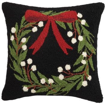 Square black pillow featuring a festive wreath of green leaves and white berries, adorned with a large red bow at the top center. The wreath design is embroidered onto the pillow.