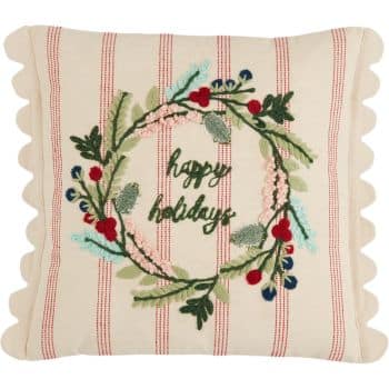 A square pillow with scalloped edges, featuring red stripes and an embroidered wreath of green leaves and red berries, with the words "happy holidays" stitched in the center.