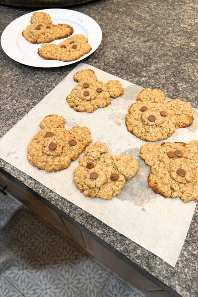 Oatmeal cookies shaped like bear faces, decorated with chocolate chips for eyes and noses, are cooling on parchment paper and a plate—these are truly my favorite Christmas cookies.