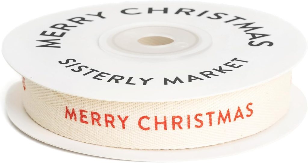 A spool of white ribbon with "MERRY CHRISTMAS" printed in red, perfect for wrapping cookies recipe gifts. The top of the spool reads "MERRY CHRISTMAS SISTERLY MARKET" in black.