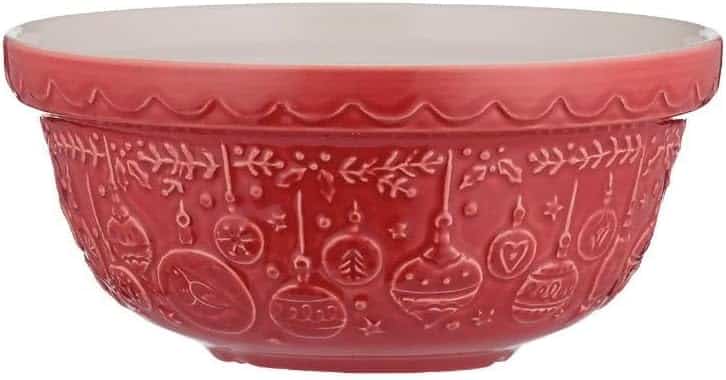 A red ceramic mixing bowl with white interior, decorated on the outside with embossed Christmas ornaments, stars, and festive patterns—perfect for preparing your favorite molded cookies recipe.
