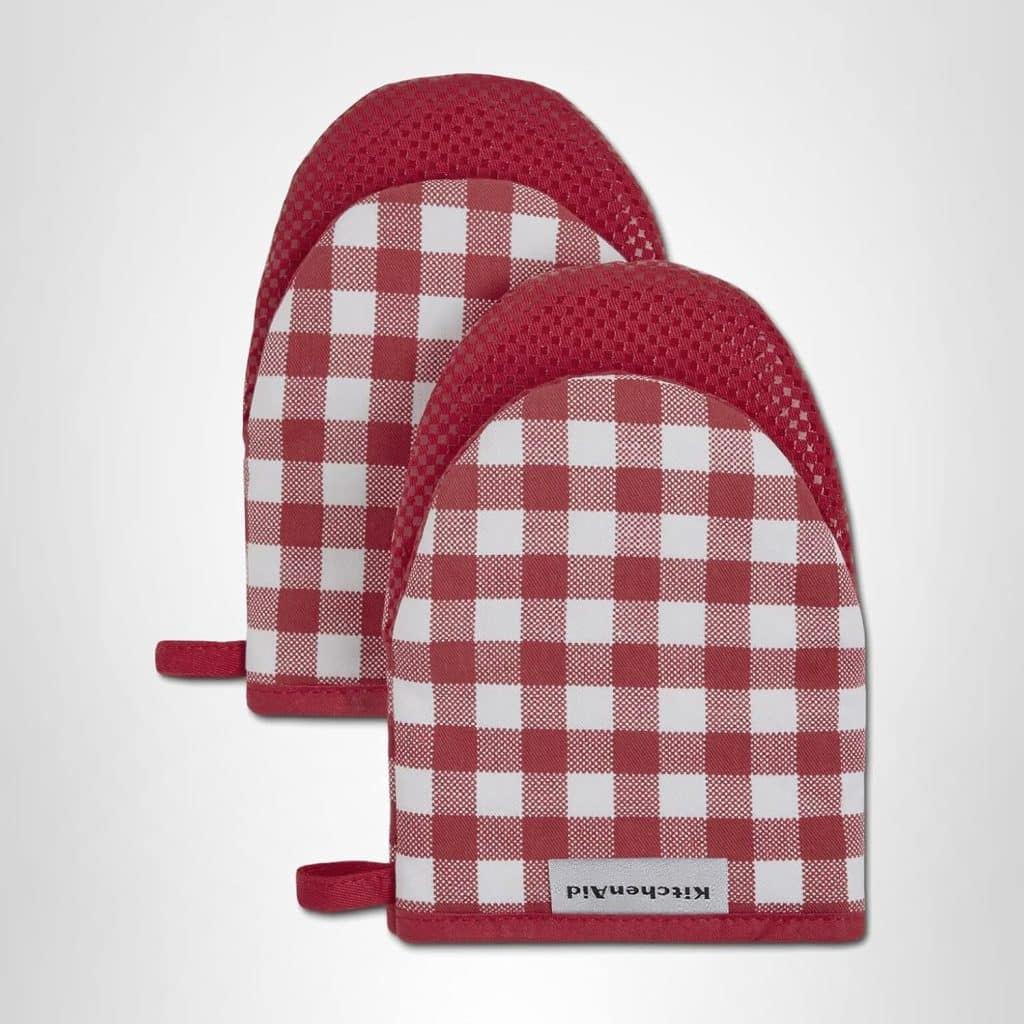 Two red and white checkered oven mitts with a textured red grip, perfect for baking your favorite molded cookies. Each mitt features handy hanging loops, and the brand name "KitchenAid" is visible on a tag at the bottom.
