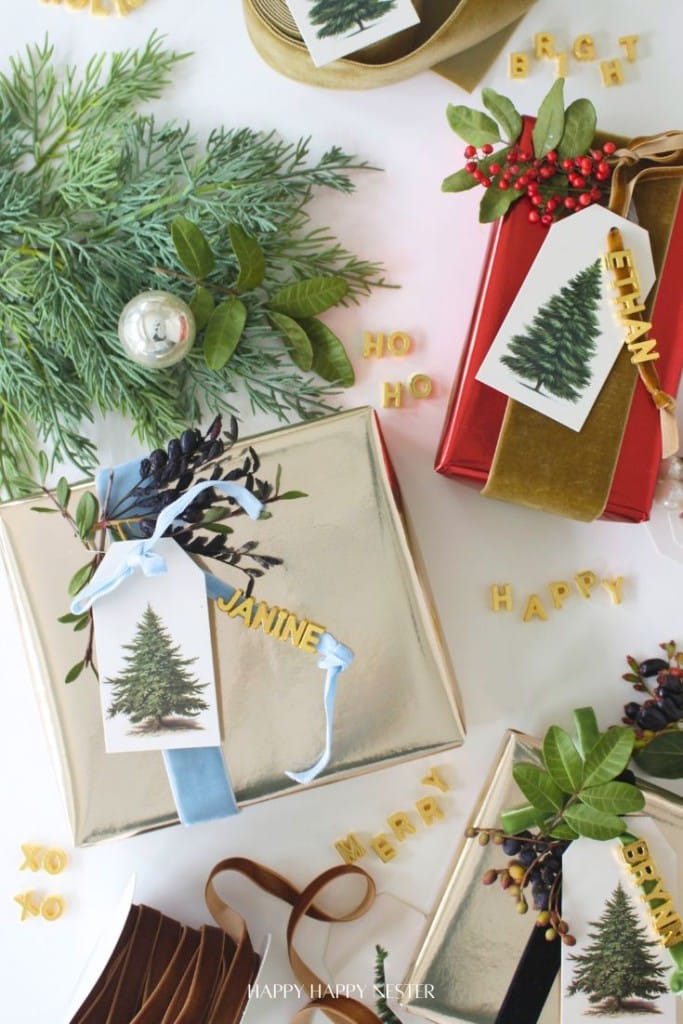Gift boxes wrapped in shiny gold and red paper are decorated with ribbons, greenery, berries, and pine tree tags. Some boxes have lettered name tags, and festive words like "HO HO" and "HAPPY" are scattered nearby.