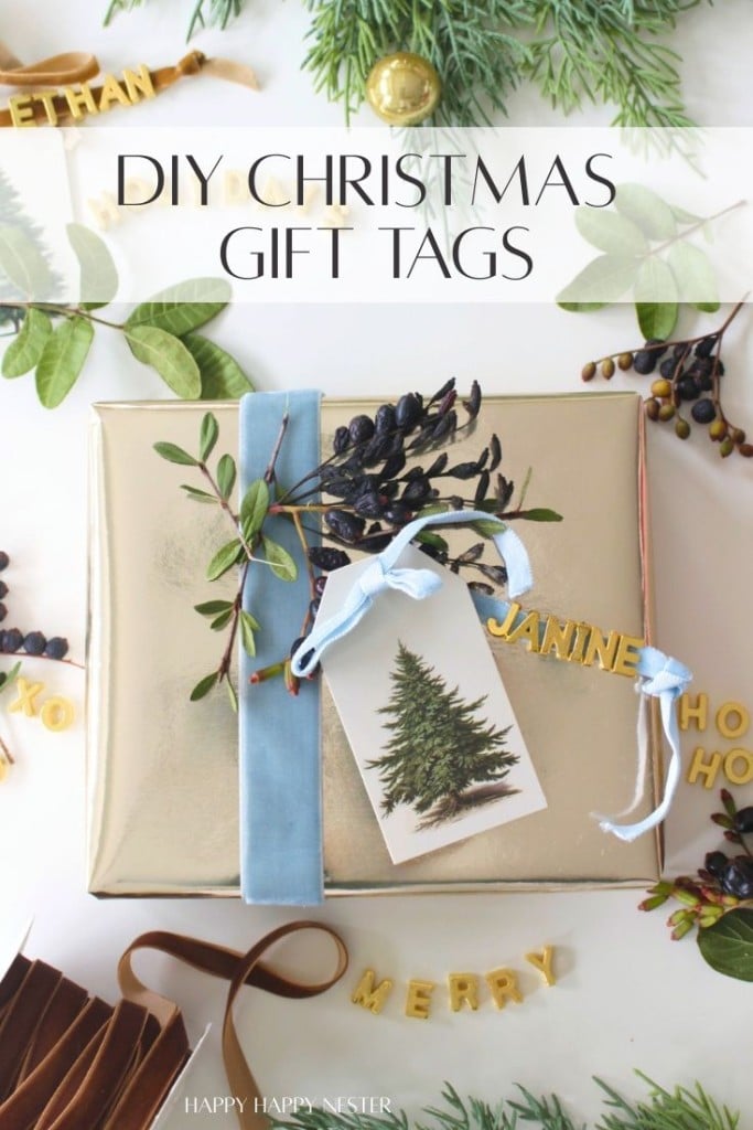 A gold-wrapped gift with a blue ribbon and pine tree tag, decorated with greenery and berries. DIY Christmas gift tags and words like "MERRY" and "HO HO HO" are scattered on a white surface with festive foliage.