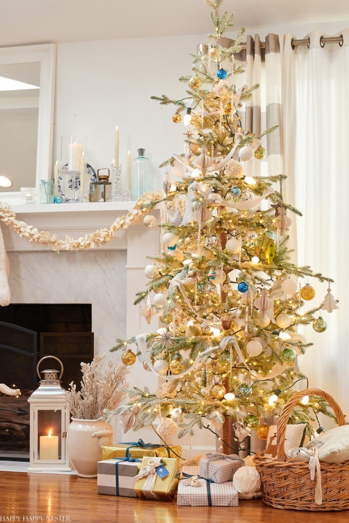 A decorated Christmas tree with white and gold ornaments stands by a fireplace—my favorite Christmas decor. Wrapped gifts, a lit lantern, and a wicker basket add to the cozy holiday scene with warm lights and neutral touches.