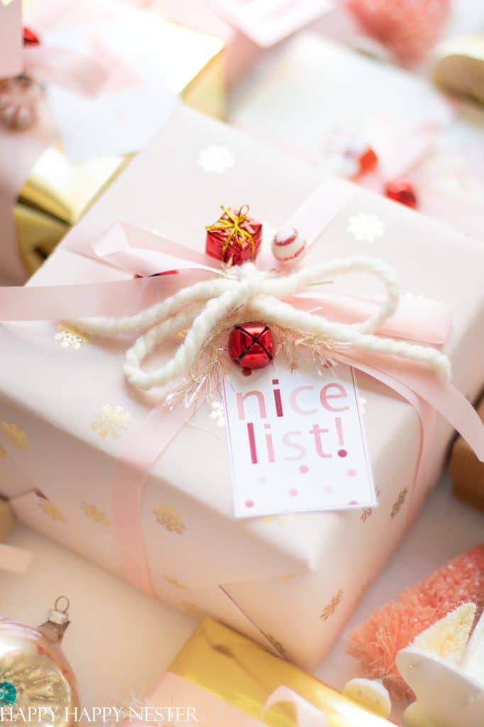 A pastel pink gift box with a white and pink ribbon, red bells, and a "nice list!" tag sits among other wrapped presents and holiday decorations—my favorite gift wrap inspiration this season.