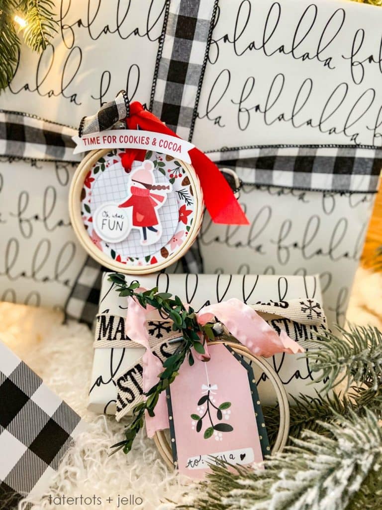 Two wrapped gifts with black and white holiday-themed paper and ribbons sit on a fluffy surface. Each, adorned with a festive tag and pine branches, captures my favorite gift wrap inspiration for the season.