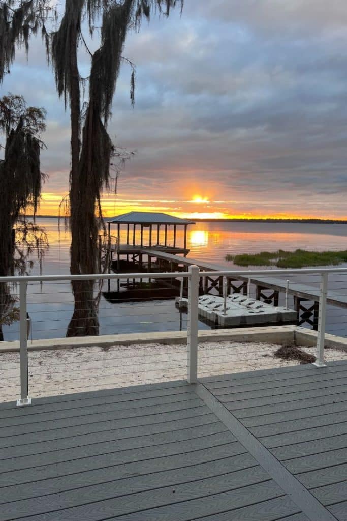 A calm lake at sunset, with a wooden dock and covered boat slip extending over the water, offers my favorite gift wrap inspiration. Spanish moss hangs from trees as the sun sets, its reflection shimmering beyond a deck railing in the foreground.