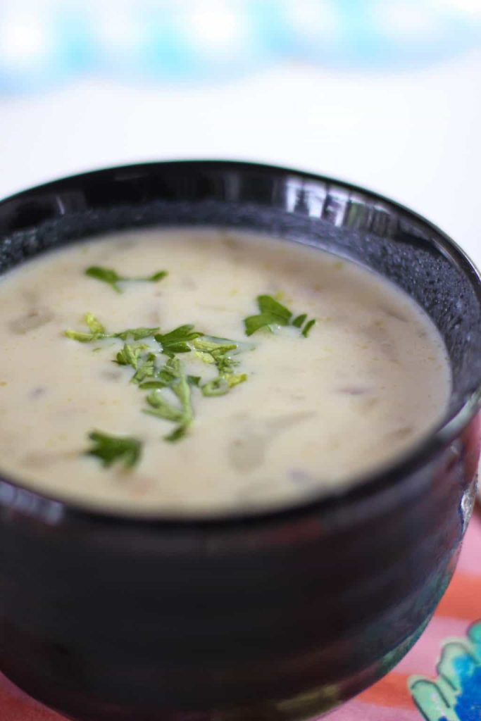 A black bowl filled with creamy white soup, garnished with chopped fresh herbs, sits on a colorful surface—perfect for anyone seeking cozy dinner ideas.