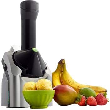 A fruit dessert maker machine beside a green bowl of fruit sorbet, bananas, a mango, a lime, strawberries, and raspberries, all on a white background.