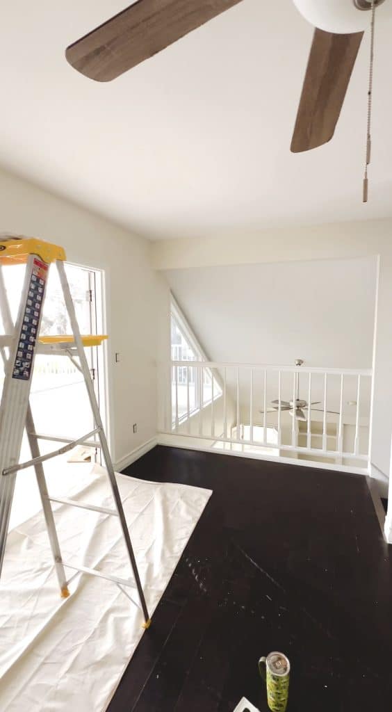 A bright room with dark wood floors, a white ceiling fan, a metal ladder, and a covered floor hint at ongoing home improvement—perfect inspiration for cozy dinner ideas while you refresh your space.