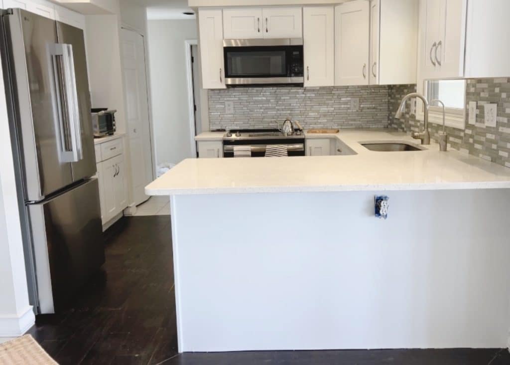 Modern kitchen with white cabinets, stainless steel appliances, a microwave above the stove, double-basin sink, and gray tile backsplash—perfect for exploring adult craft ideas or preparing pink crafts on the spacious island counter with an electrical outlet.