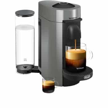 A silver Nespresso coffee machine brewing espresso into a glass cup, with another empty glass cup beside it. A transparent water reservoir is attached to the back of the machine.