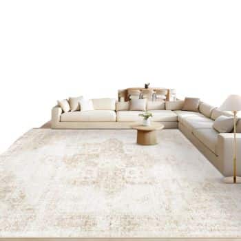 A modern living room with a large L-shaped beige sofa, a round wooden coffee table, a floor lamp, and a light-colored textured rug on the floor. Small plants and cushions add decor to the space.