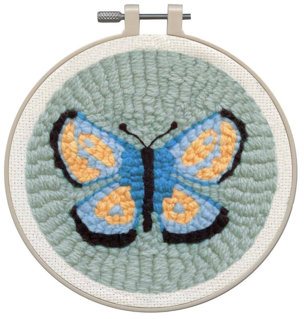 A round embroidery hoop holds needlework featuring a colorful butterfly with blue, orange, and black wings on a light green background—perfect for punch needle crafting or DIY decor projects.
