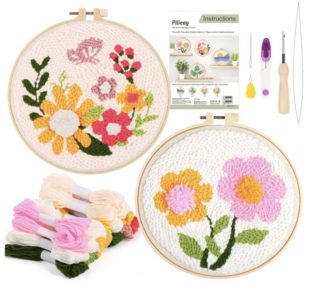 Two finished punch needle crafting hoops with colorful flower designs, embroidery threads in pink, yellow, and green, metal tools, and a diy instruction booklet displayed on a white background.