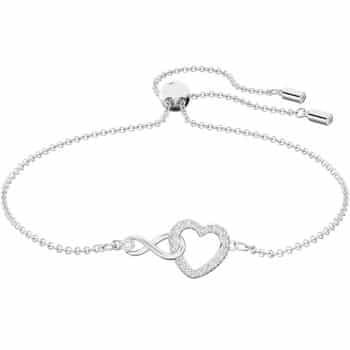 A delicate silver bracelet with an adjustable chain, featuring an intertwined infinity symbol and a heart encrusted with small, sparkling stones at the center.