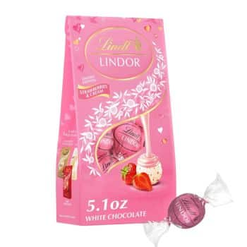 A pink bag of Lindt Lindor Strawberries & Cream white chocolate truffles, with images of truffles, strawberries, and cream on the packaging. One wrapped truffle is shown in front of the bag. The bag weighs 5.1 oz.