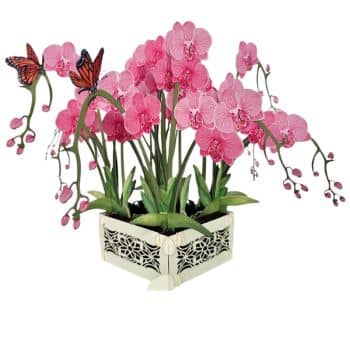 A decorative arrangement of pink orchids with two orange butterflies perched on the flowers, set in an ornate white corner planter with a floral cutout design.