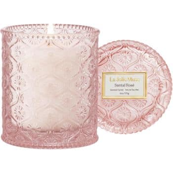 A pink textured glass candle jar labeled "Santal Rosé" with the matching lid resting beside it. The candle inside the jar is unlit.