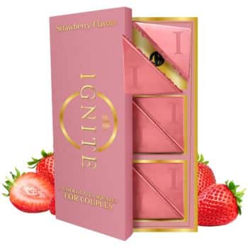 A pink box labeled "Ignite Strawberry Flavour" with three chocolate squares partially unwrapped inside, surrounded by fresh strawberries, marketed as chocolate for couples.