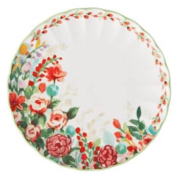 A round plate with a scalloped edge, featuring a colorful floral pattern of red, pink, and green flowers and leaves decorating one side of the rim. The rest of the plate is white.