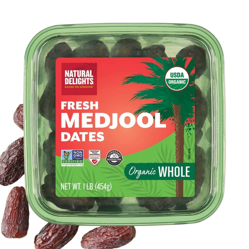 A green plastic container of Natural Delights Fresh Medjool Dates, labeled USDA Organic, Organic Whole, Non-GMO, and weighing 1 lb (454g). Perfect for snacking or adding to a chocolate covered quinoa recipe. Several dates are shown outside the container.