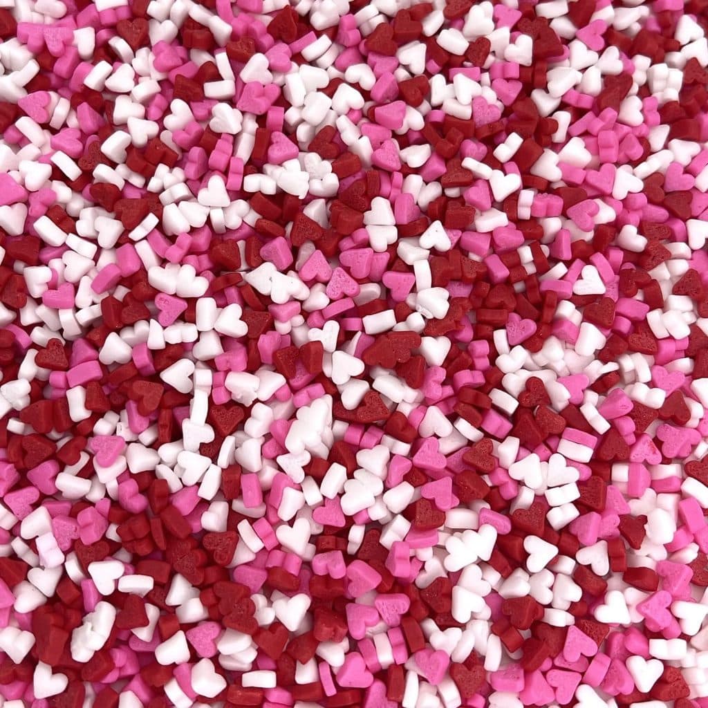 A close-up view of numerous small heart-shaped sprinkles in shades of pink, red, and white, densely scattered like the perfect topping for a heart shaped brownies recipe.