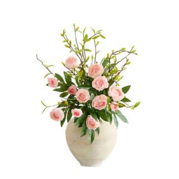 A white ceramic vase filled with pink rose flowers and green leafy branches, arranged against a plain white background.