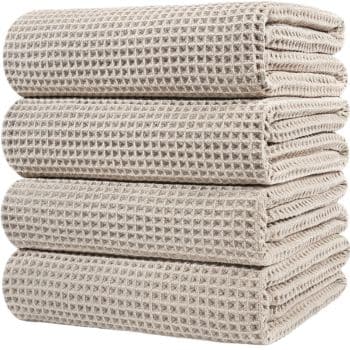 Four neatly folded beige waffle-weave towels stacked on top of each other, showing their textured grid pattern.