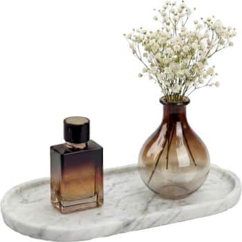 A small marble tray holds a dark glass perfume bottle and a round glass vase with white baby's breath flowers arranged inside.