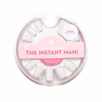 A circular package of press-on nails labeled "The Instant Mani." The nails are pale with small white dots. The label notes the nails are extra short.