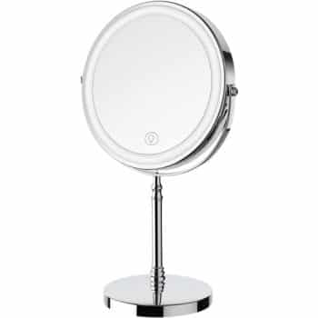 A round, freestanding tabletop vanity mirror with a silver frame and base, featuring a touch button on the surface, likely for built-in lighting.