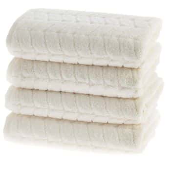 Four neatly folded, fluffy white towels stacked on top of each other, with a subtle textured pattern visible on the surface.