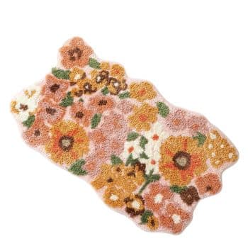 Irregularly shaped rug with a floral design in shades of orange, yellow, brown, and green on a light background. The rug features various flowers and greenery in a textured, tufted style.