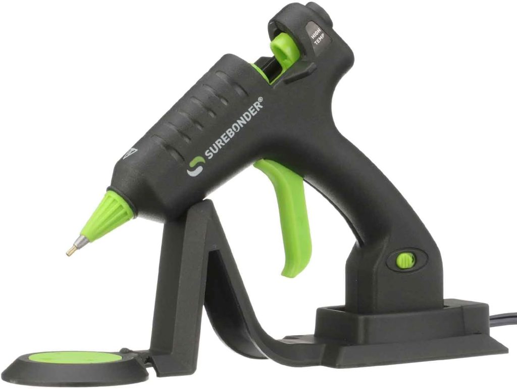 A black and green Surebonder hot glue gun rests on a matching stand, ready to help you craft your next spring flower wreath, with its visible power switch and pointed glue nozzle.